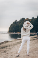 blonde girl in a white hat walks along the seashore on an autumn day - 527368106