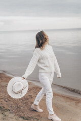 blonde girl in a white hat walks along the seashore on an autumn day - 527368120