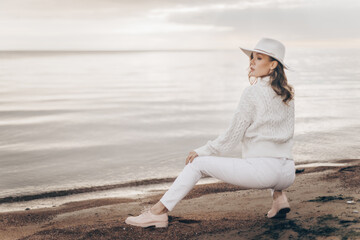 blonde girl in a white hat walks along the seashore on an autumn day - 527368123