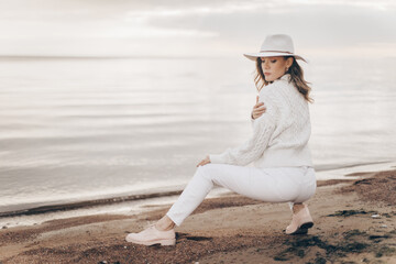 blonde girl in a white hat walks along the seashore on an autumn day - 527368145