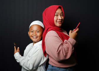 A child and his mother are playing on each other's cellphone looking at the camera isolated on black background.