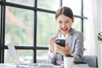 Exciting, successful Asian businesswoman. Excited to win with smartphones in the office at work.