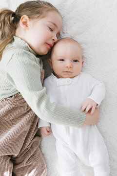 Girl (2-3) embracing newborn (0-1&nbsp;months)&nbsp;brother on bed