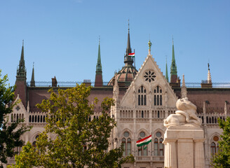Fototapeta premium You see the spires and roof line of the Parliament building in Budapest Hungary. There in front of the building is the lion statue and the Hungarian flag is in the air.