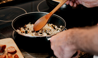 Man hands cooking rice and vegetables in a pan
