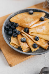 
pancakes on a plate, sprinkled with powdered sugar, with berries. near a small sieve, berries and eggs. light background