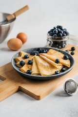 
pancakes on a plate, sprinkled with powdered sugar, with berries. near a small sieve, berries and eggs. light background
