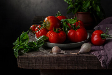 Fresh tomatoes, basil and garlic on a rustic table against a dark background