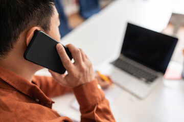 Unrecognizable Japanese Businessman Talking On Phone Using Laptop At Workplace
