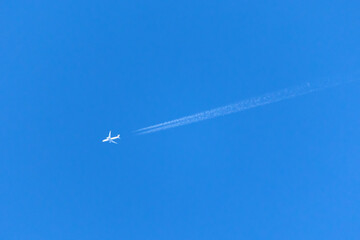 A plane crossing the blue sky leaving a white trail.