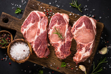 Pork meat, raw pork steaks on cutting board with ingredients for cooking. Top view with copy space.