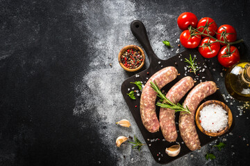 Bratwurst or sausages on cutting board with spices at black table. Ready for cooking. Top view with copy space.