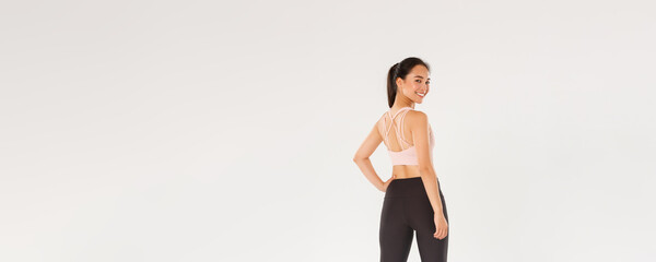 Full length of smiling slim and strong female fitness coach, female athelte in sportswear turn behind to look at camera with pleased, motivated expression, girl ready for workout, white background