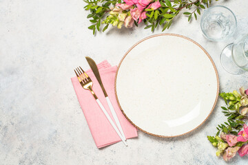 Table setting with white plate, flowers and cutlery at white kitchen table. Top view with copy space. - obrazy, fototapety, plakaty