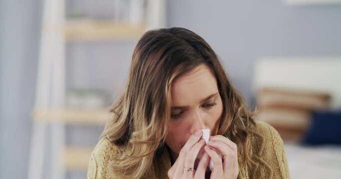 Covid, sick or cold person blowing nose, sneeze with tissue and ill virus while sitting in the lounge. Woman suffering from allergies, virus or disease with flu symptoms in the living room at home