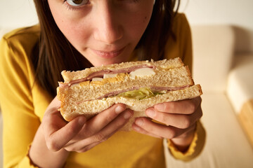 Teenage girl holding and smelling a sandwich with ham and eggs