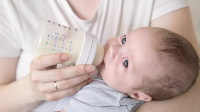 loving mother feeding her little boy child with milk baby bottle at home, portrait infant Baby eating, drinking powdered milk