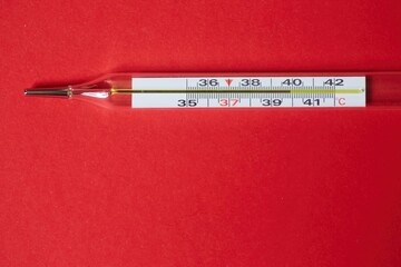 The classic mercury thermometer with a scale of degrees Celsius and high temperature lies on a red...