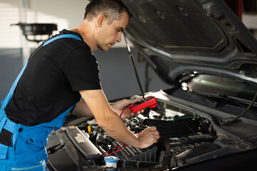 Professional car mechanic check battery voltage with electric multimeter. Automobile diagnosis. Car mechanic repairer looks for engine failure on diagnostics equipment in vehicle service workshop