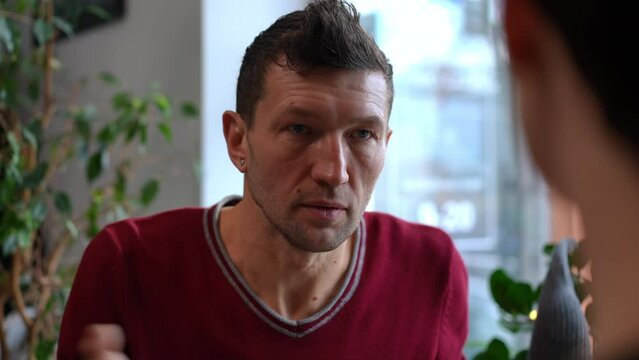 Portrait of serious adult man excusing as female hand raising at front. Guilty Caucasian husband boyfriend explaining himself to wife girlfriend in cafe. Conflict and breakup concept