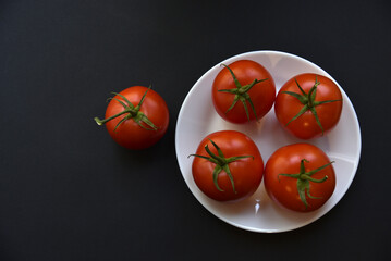 Red juicy tomatoes on a white plate. Delicious tomatoes on a black background.