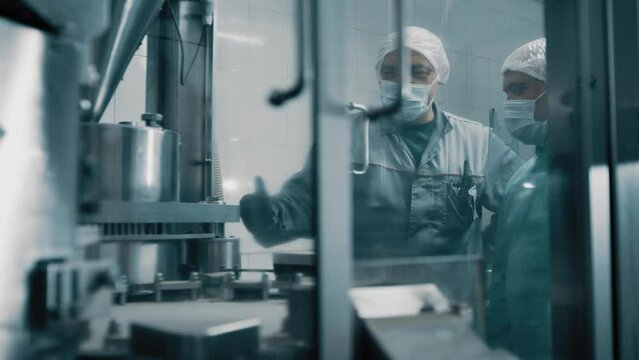 4K Machine operators working on a pharmaceutical production line discussing the production process. Automatic capsule filling machine. Automatic production line in a pharmaceutical company