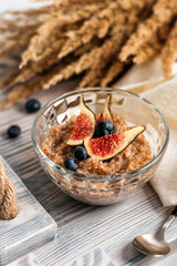 
wheat porridge with figs and blueberries on a wooden rack, next to a spoon and dry plants