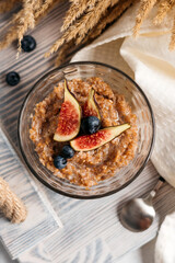 
wheat porridge with figs and blueberries on a wooden rack, next to a spoon and dry plants
