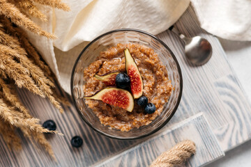 
wheat porridge with figs and blueberries on a wooden rack, next to a spoon and dry plants