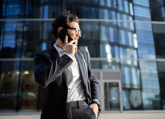 A male business manager in a business suit uses a phone, goes to the office