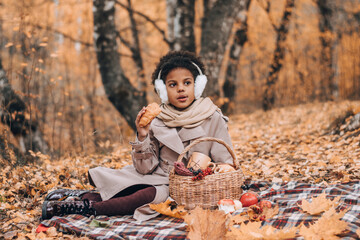 Little African-American girl eats a croissant at a picnic in an autumn park.Diversity,autumn...