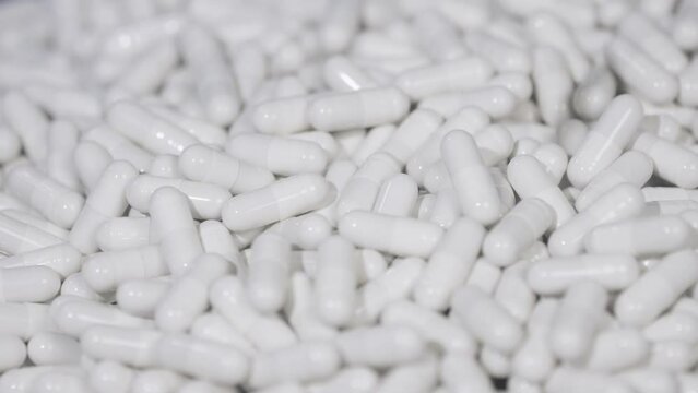 Pills capsules falling onto the surface of the tablets in slow motion. Medicine Capsules. Healthcare and pharmaceutical production concept. Close up, DOF, 4K video