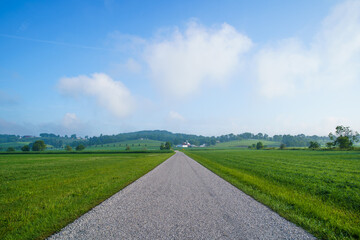 Straight country road through flat farm fields in Amish country, Ohio with rolling hills in the distance in summer