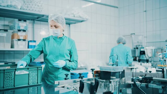 4K women work on the capsule packaging line and put the finished product into a box. Bottle filling machine. Bottles on a conveyor belt. Production line of pharmaceutical manufacturing. Slow motion