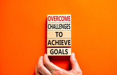 Overcome challenges to achieve goals symbol. Concept words Overcome challenges to achieve goals on wooden blocks on a beautiful orange background. Businessman hand. Business goals concept. Copy space.