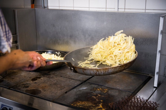 Cropped hands of chef sauteing onions in kitchen of restaurant