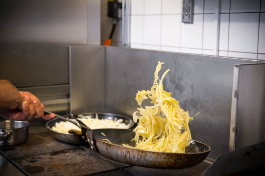 Chef Tossing Onions In Cooking Pan At Commercial Kitchen