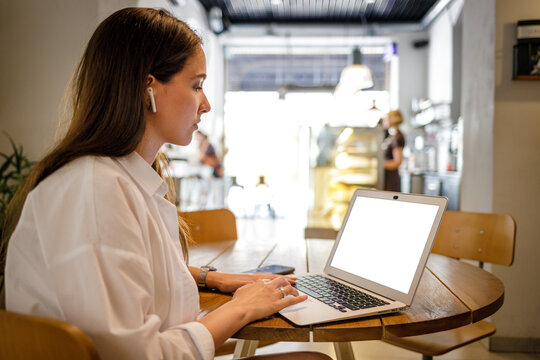 Young pretty woman using laptop in cafe. Mock up image with blank screen of the laptop