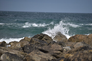 Das Meer ist wellig und bricht wild mit spritzendem Wasser und Gischt an rauen und dunklen Steinen in der französischen Region Bretagne