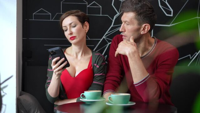 Selfish woman surfing Internet on smartphone ignoring man sitting in cafe. Sad Caucasian adult boyfriend sighing looking away as arrogant girlfriend disregarding partner. Bad date concept