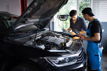 Car service employees inspect car's engine bay with a LED lamp. Manager checks tasts on tablet computer and explains an Engine breakdown to an male mechanic. Auto service