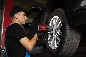 Mechanic is Unscrewing Lug Nuts with Pneumatic Impact Wrench. Repairman Works in a Modern Car Service. Specialists Removes the Wheel in Order to Fix a Component on a Vehicle