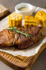 Fried pork loin with sauce and grilled corn on the board on brown concrete table macro close up vertical