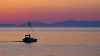 A yacht sailing towards the mountains on the horizon. the sky and the sea are painted red before sunrise. A girl takes a selfie on a yacht.