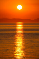 Reflection of the sun rising from behind the mountains on the horizon on the surface of sea water.