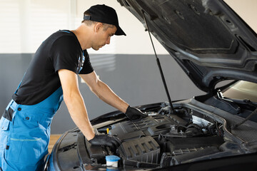 Fototapeta na wymiar Mechanic man open a car hood and check up the engine. Car mechanic noting repair parts during open car hood engine repair at garage. Overheating of a car engine. Motor with open hood