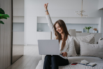 Successful young female entrepreneur talking via internet with partner rising up hand with thumb up, smiling making video call at home, sittingg on couch, using laptop. Business and remote education.