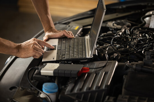Specialist inspecting the vehicle in order to find broken components and errors in data logs. Automobile service, car mechanic. Auto mechanic uses a laptop while conducting diagnostics test