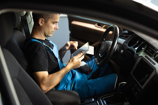 Using digital tablet for car diagnostic. Interactive diagnostics software on an advanced computer. Mechanic using tablet pc at the repair garage service