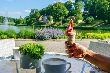 Ice cream in a waffle in a woman's hand with painted nails on the background of a summer landscape